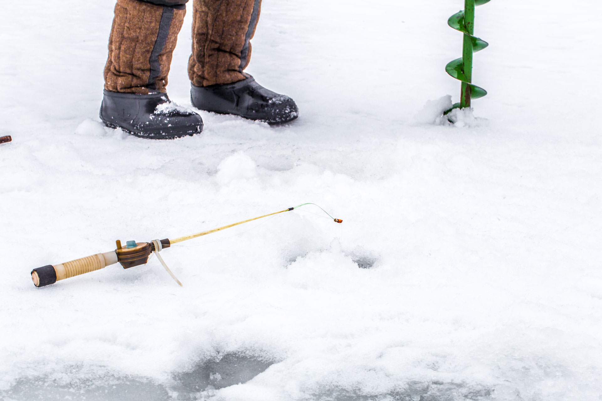 Ice fisherman standing on frozen lake with fishing rod and equipment near holes in ice