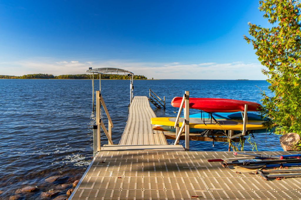 Wooden dock with colorful kayaks and paddleboards on calm blue water under clear sky