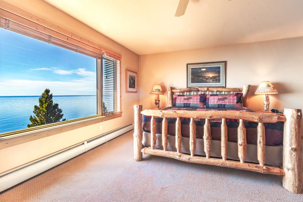 Luxurious bedroom with panoramic ocean view window, wooden bed frame, nightstands with lamps, and coastal decor